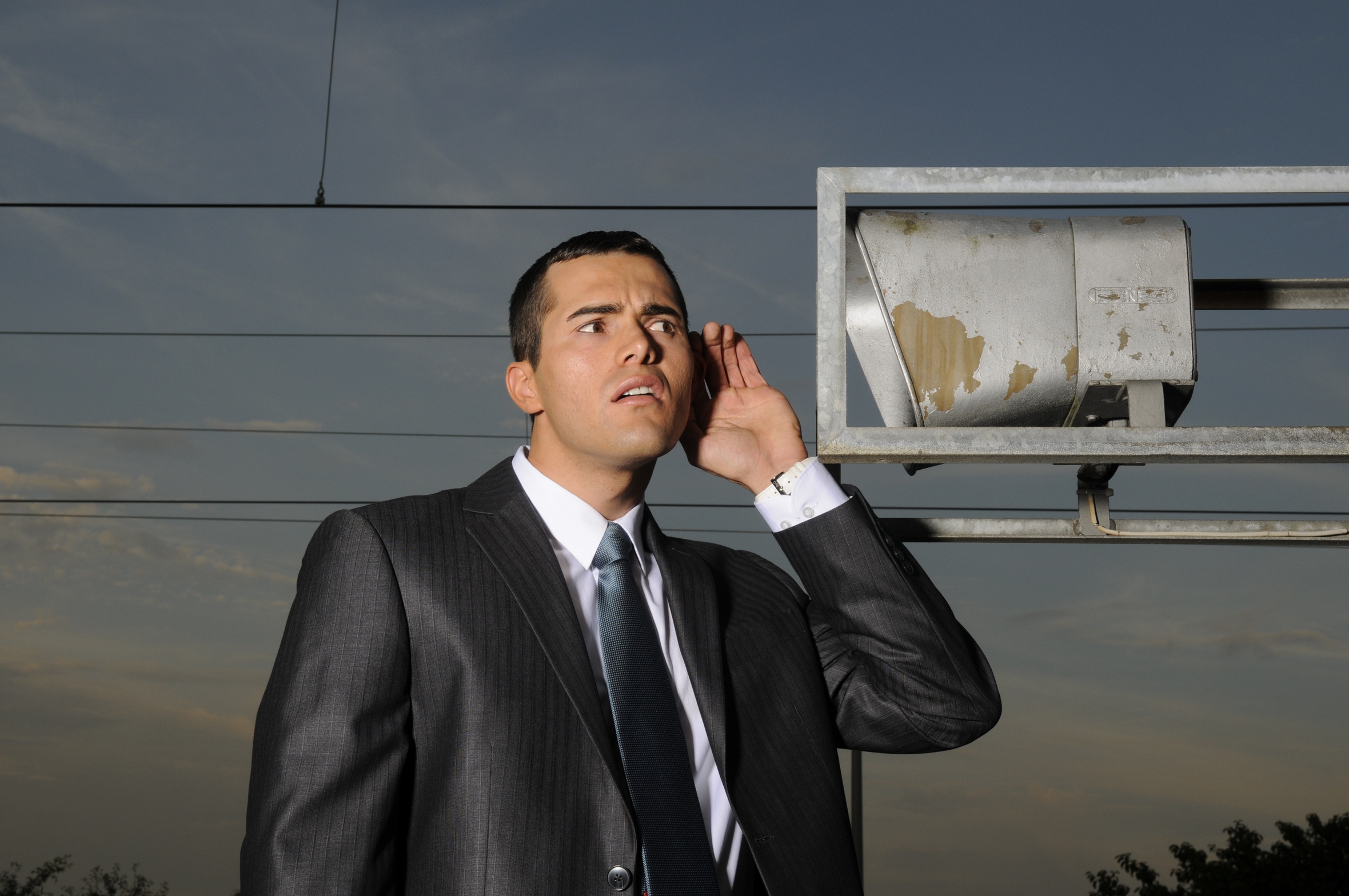 Mann im Anzug steht im Freien und hört aufmerksam zu, symbolisch für Sprachalarmanlagen und die Bedeutung klarer Alarm- und Evakuierungsdurchsagen im Brandschutz.